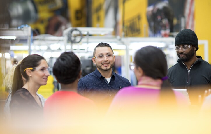 diverse group of employees meeting in manufacturing facility wearing ppe