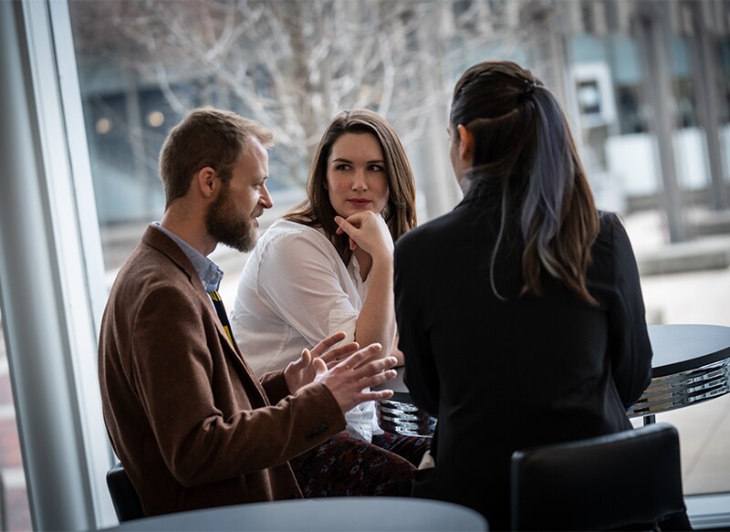 Three employees sit at a table deep in conversation