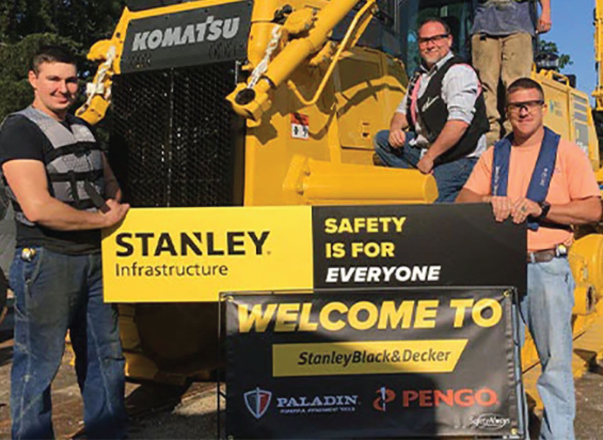 Stanley Black & Decker employees standing in front of heavy machinery while holding a banner welcoming PALADIN and Pengo to the company