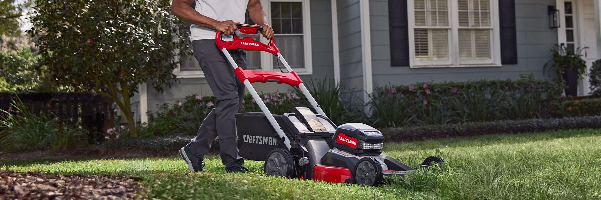 Craftsman CMCMWSP320X2 lawn mower in use on grass lawn in front of a gray house.